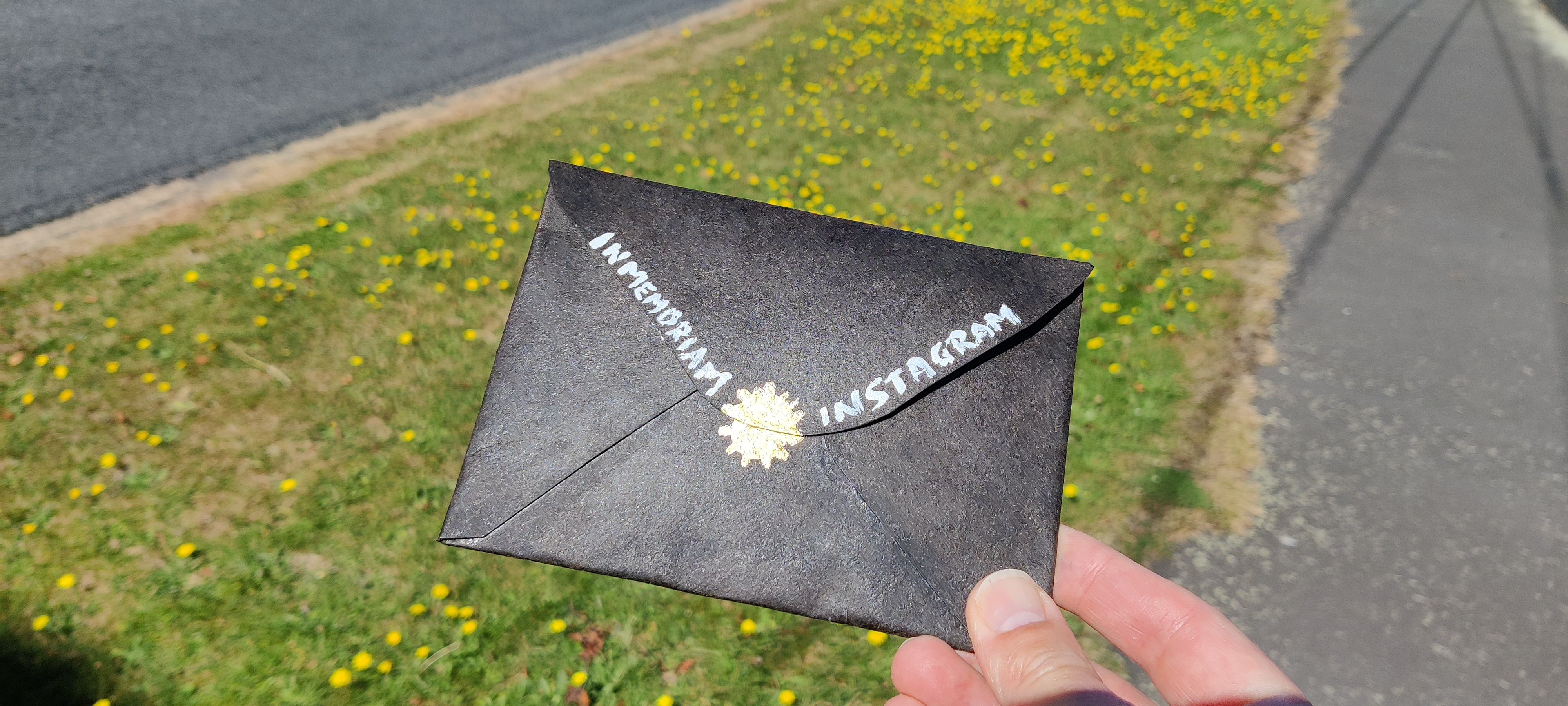 Black envelope with painted white letters reading: In Memoriam Instagram